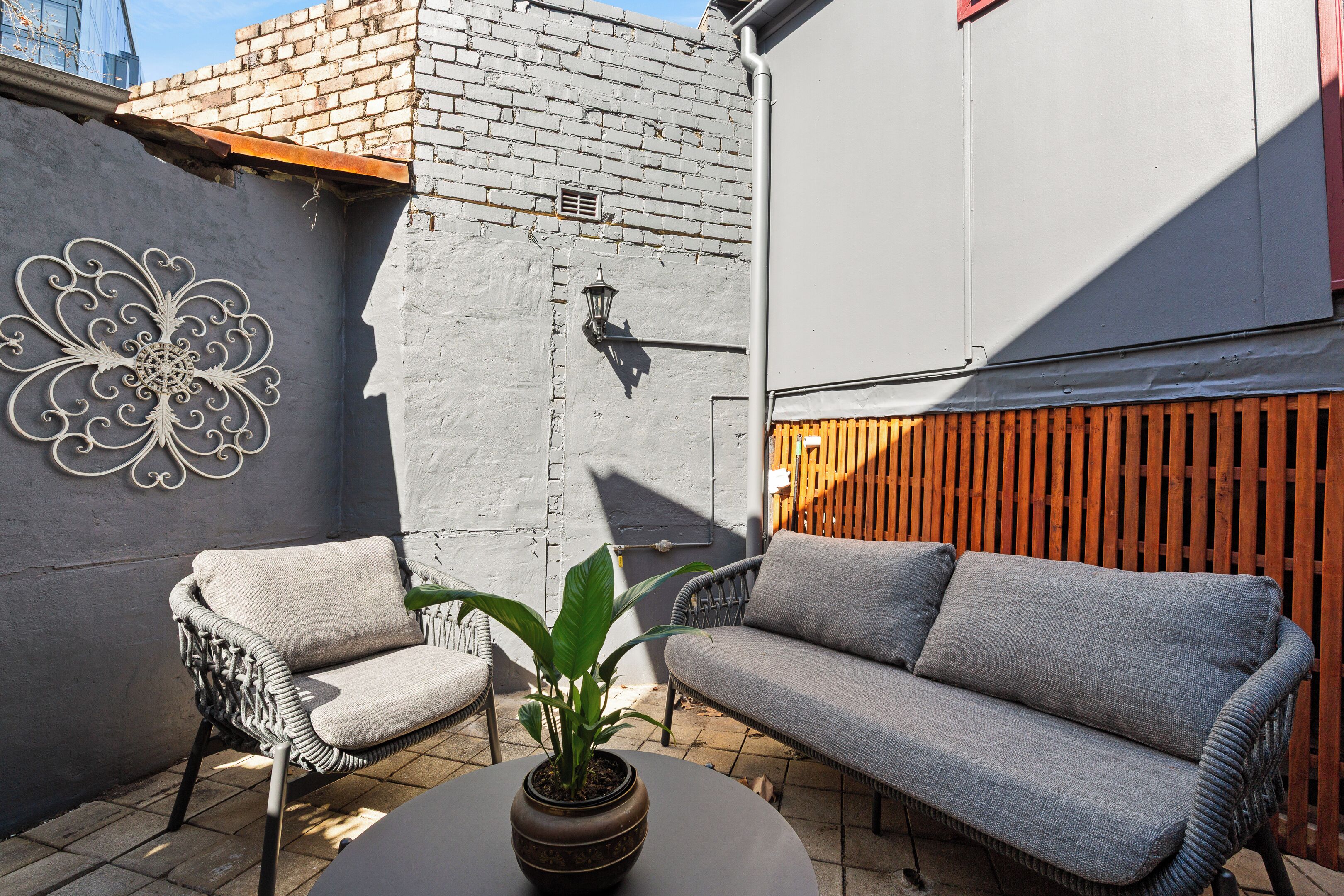 A patio with a grey sofa, a wicker chair, and a potted plant.