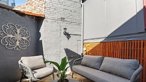 Un patio con un divano grigio, una sedia in vimini e una pianta in vaso.