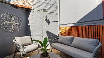 A patio with a grey sofa, a wicker chair, and a potted plant.