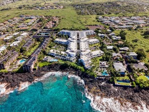 An aerial view of a coastal resort with multiple buildings, a rocky shoreline, and clear blue waters. - Royal Seacliff#401 (Kailua-Kona)