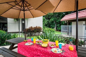 An outdoor dining area with a picnic table set for two, covered by a large umbrella. - Kona Mansions#b116 Mountain Views, No Stairs! (Kailua-Kona)