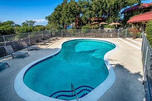 A swimming pool with a curved edge, surrounded by lounge chairs and a fence. - Kona Mansions#b116 Mountain Views, No Stairs! (Kailua-Kona)