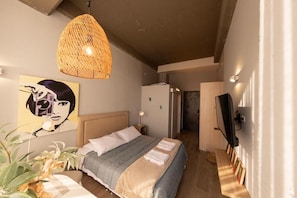 Ein Schlafzimmer mit einem Bett, einer Pendelleuchte, einem Fernseher und einer Tür zu einem anderen Raum.