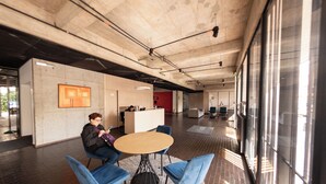 A modern interior with a round table and blue chairs, a reception desk, and large windows. - Studio artístico Chapinero Alto Zona G (Bogotá)