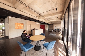 A modern interior with a round table and blue chairs, a reception desk, and large windows. - Studio artístico Chapinero Alto Zona G (Bogotá)