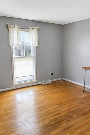 A room with a large window, wooden flooring, and a power outlet on the wall.