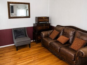 A living room with a brown leather sofa, a grey armchair, and a wooden chest of drawers.