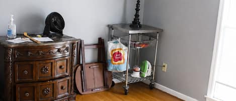 Una habitación con piso de madera, un aparador, una lámpara, un ventilador y un saco de pan.