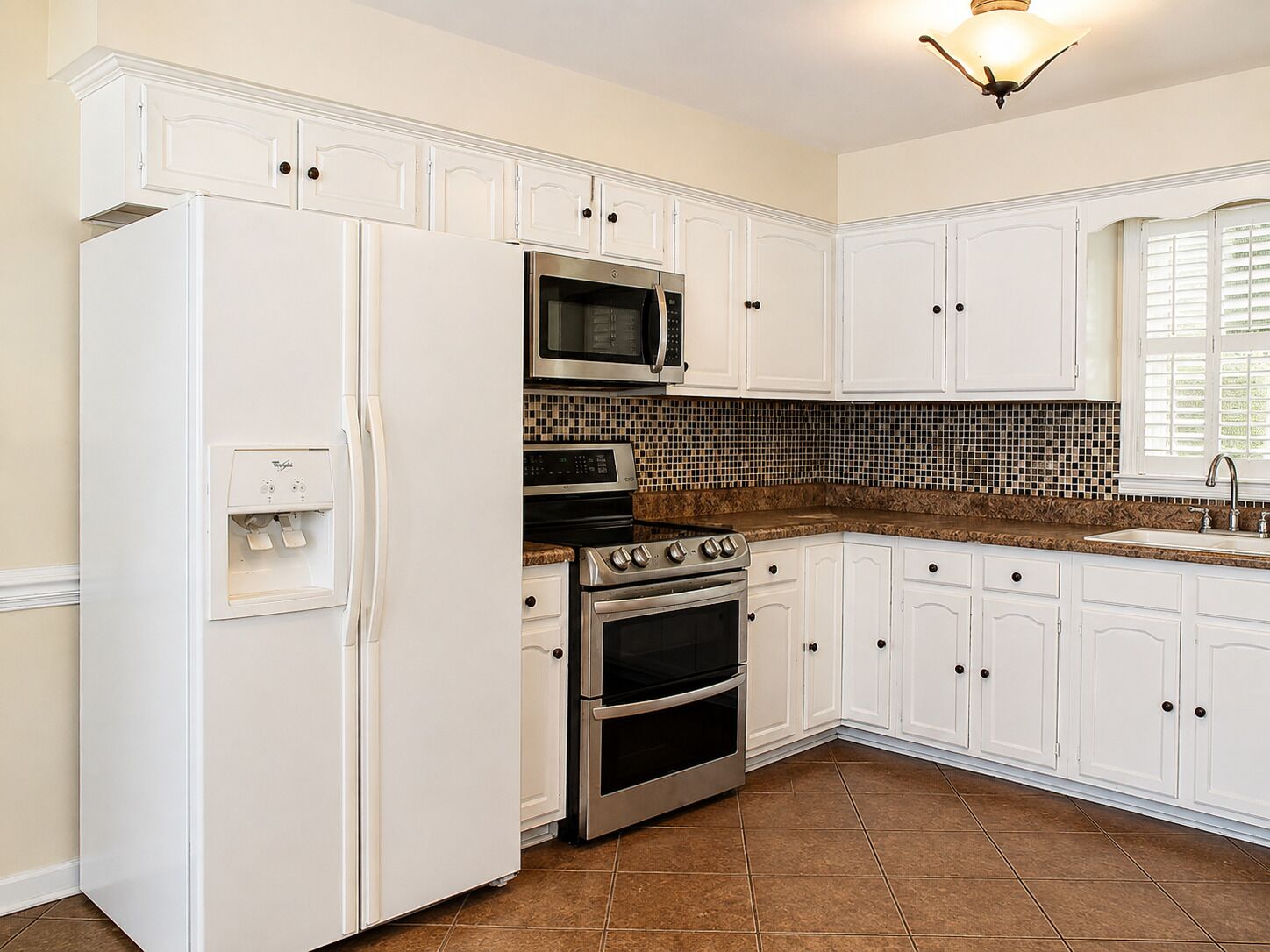 A kitchen with white cabinets, a refrigerator, a microwave, an oven, and a tiled backsplash.