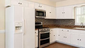 A kitchen with white cabinets, a refrigerator, a microwave, an oven, and a tiled backsplash.