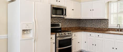 A kitchen with white cabinets, a refrigerator, a microwave, an oven, and a tiled backsplash.