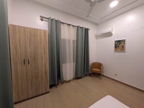 A room with a wardrobe, a chair, a ceiling fan, and a wall-mounted air conditioner.
