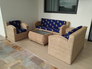 A wicker sofa set with a glass coffee table, positioned on a tiled floor with a view of a window.