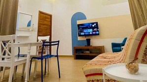 A modern living room with a flat-screen TV, ceiling fan, and a dining area with chairs and a table. - Petit Hùéfà - Apartment for 2 people (Ouidah)