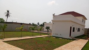 A modern two-story house with a paved courtyard, surrounded by a low wall and small palm trees. - Petit Hùéfà - Apartment for 2 people (Ouidah)