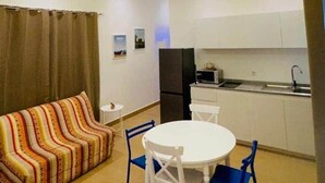 A compact living space with a sofa, dining table, chairs, a ceiling fan, and a kitchenette. - Petit Hùéfà - Apartment for 2 people (Ouidah)