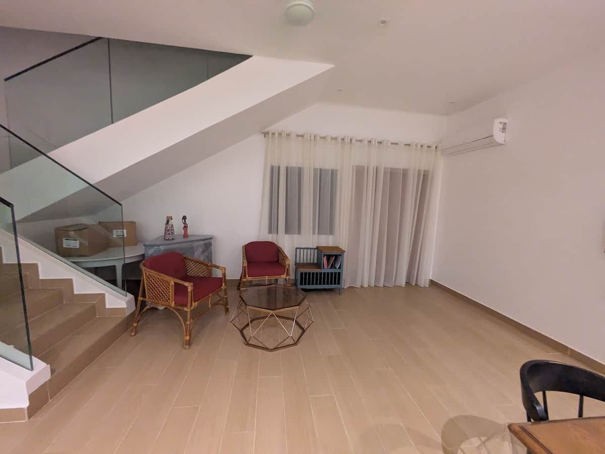 Una sala moderna con una escalera de vidrio, un comedor con mesa y sillas, y un mueble azul.