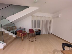 A modern living room with a glass staircase, a dining area with a table and chairs, and a blue cabinet.
