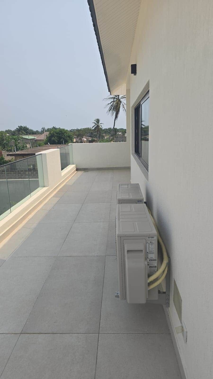 Een balkon met een glazen hekwerk, een raam en een airconditioner.