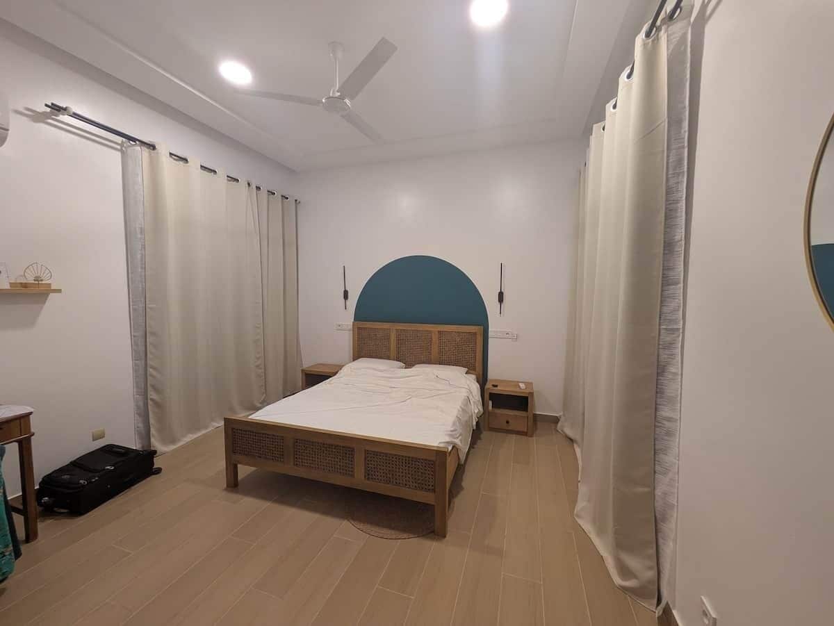 A bedroom with a bed, bedside tables, a ceiling fan, and curtains.