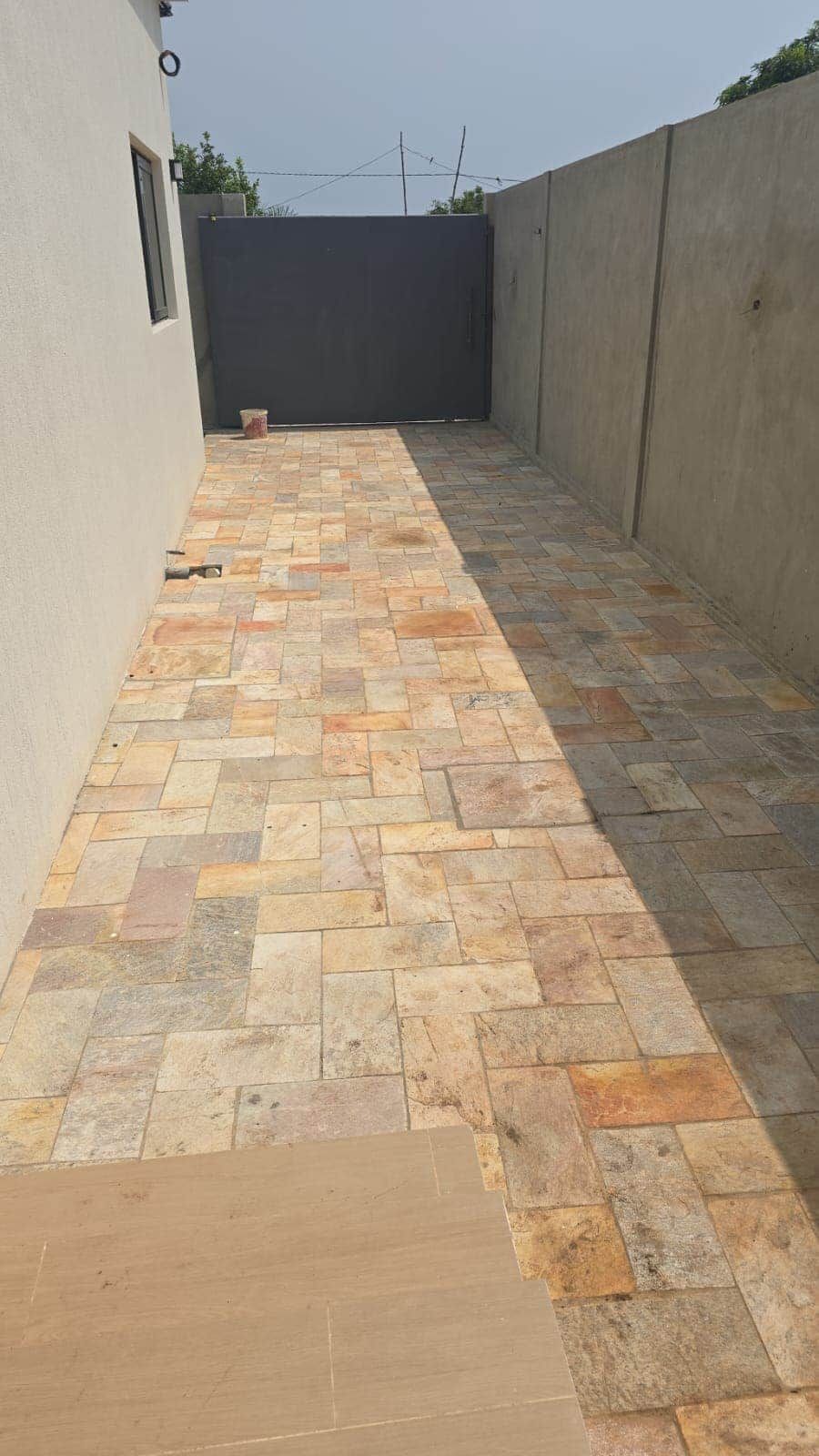 Un espacio al aire libre con suelo empedrado, una pared de concreto y una ventana a la izquierda.