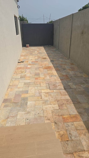 A paved outdoor area with a concrete wall and a window on the left.