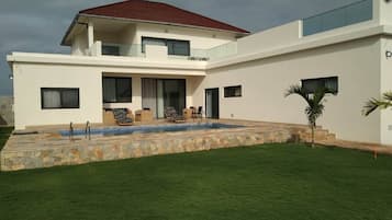 A modern two-story house with a swimming pool, a covered patio, and a well-maintained lawn.
