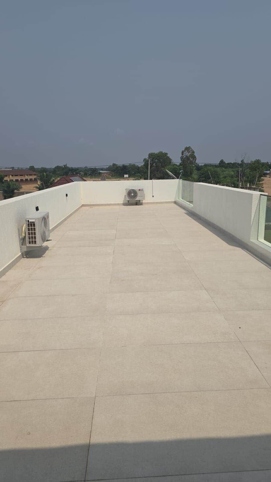 Una terraza plana en la azotea con vistas despejadas del paisaje circundante, que incluye árboles y edificios.