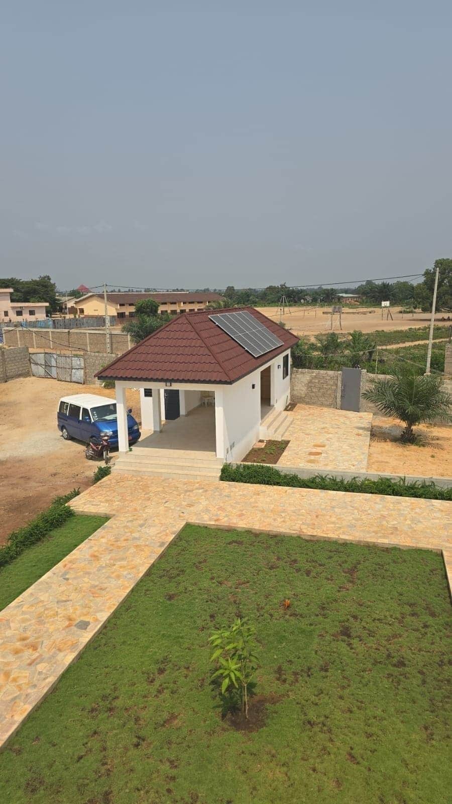 A residential property with a paved driveway, a small house with a tiled roof, and a parked blue vehicle.