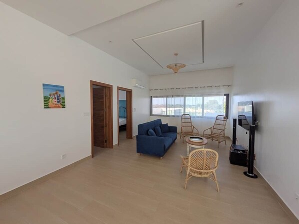 An open-plan living area with a sofa, chairs, a television, and a view through the window.