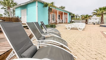 Un área de descanso frente a la playa con sillones de sol y un pequeño edificio de color azul.