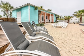 Un área de descanso frente a la playa con sillones de sol y un pequeño edificio de color azul.