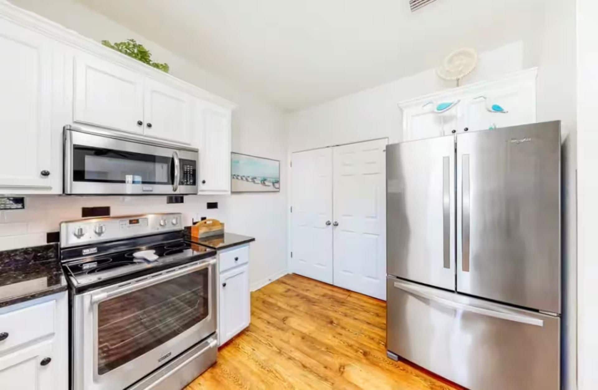 Una cocina moderna con armarios blancos, un refrigerador de acero inoxidable, un microondas y un horno.