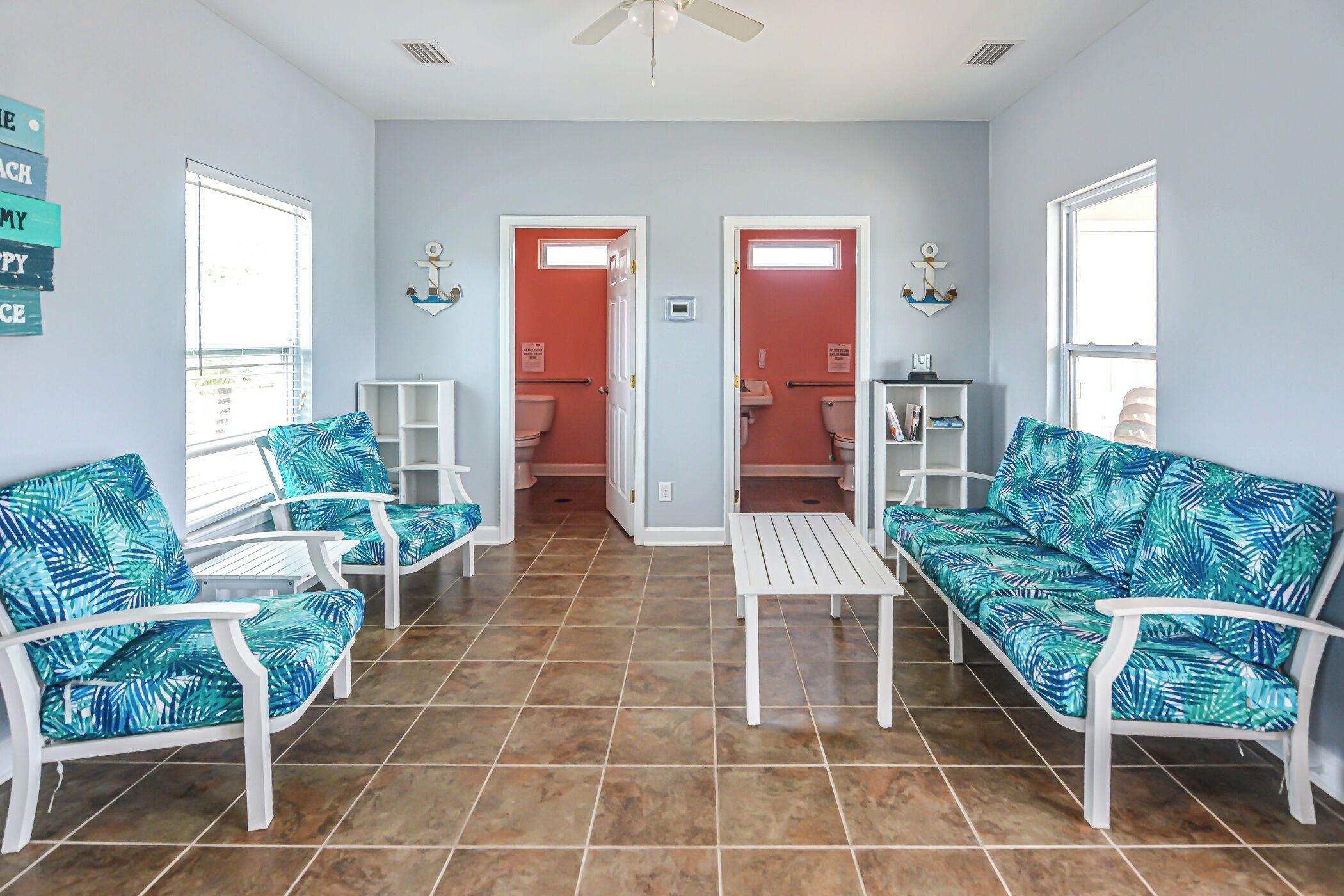 Una habitación con dos sofás blancos con estampado tropical azul, una mesa de centro blanca y un suelo de baldosas.