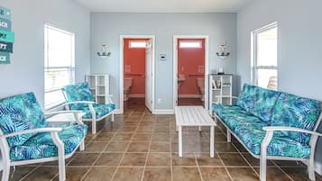 Una habitación con dos sofás blancos con estampado tropical azul, una mesa de centro blanca y un suelo de baldosas.