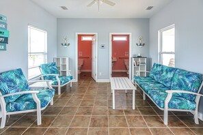 Una habitación con dos sofás blancos con estampado tropical azul, una mesa de centro blanca y un suelo de baldosas.