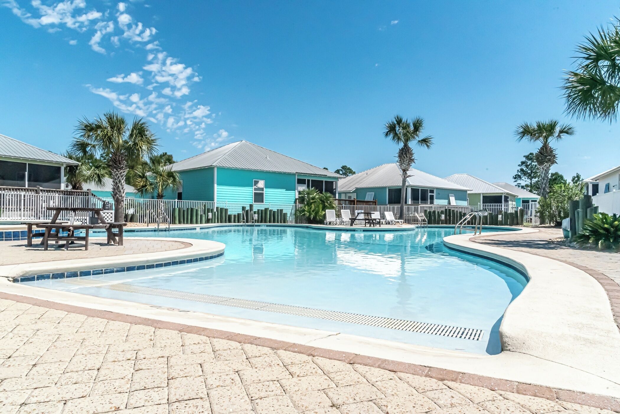 A swimming pool with lounge chairs and palm trees, surrounded by buildings with a light blue exterior.