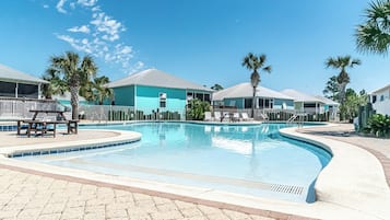 Una piscina con sillas de descanso y palmeras, rodeada de edificios con fachada azul claro.