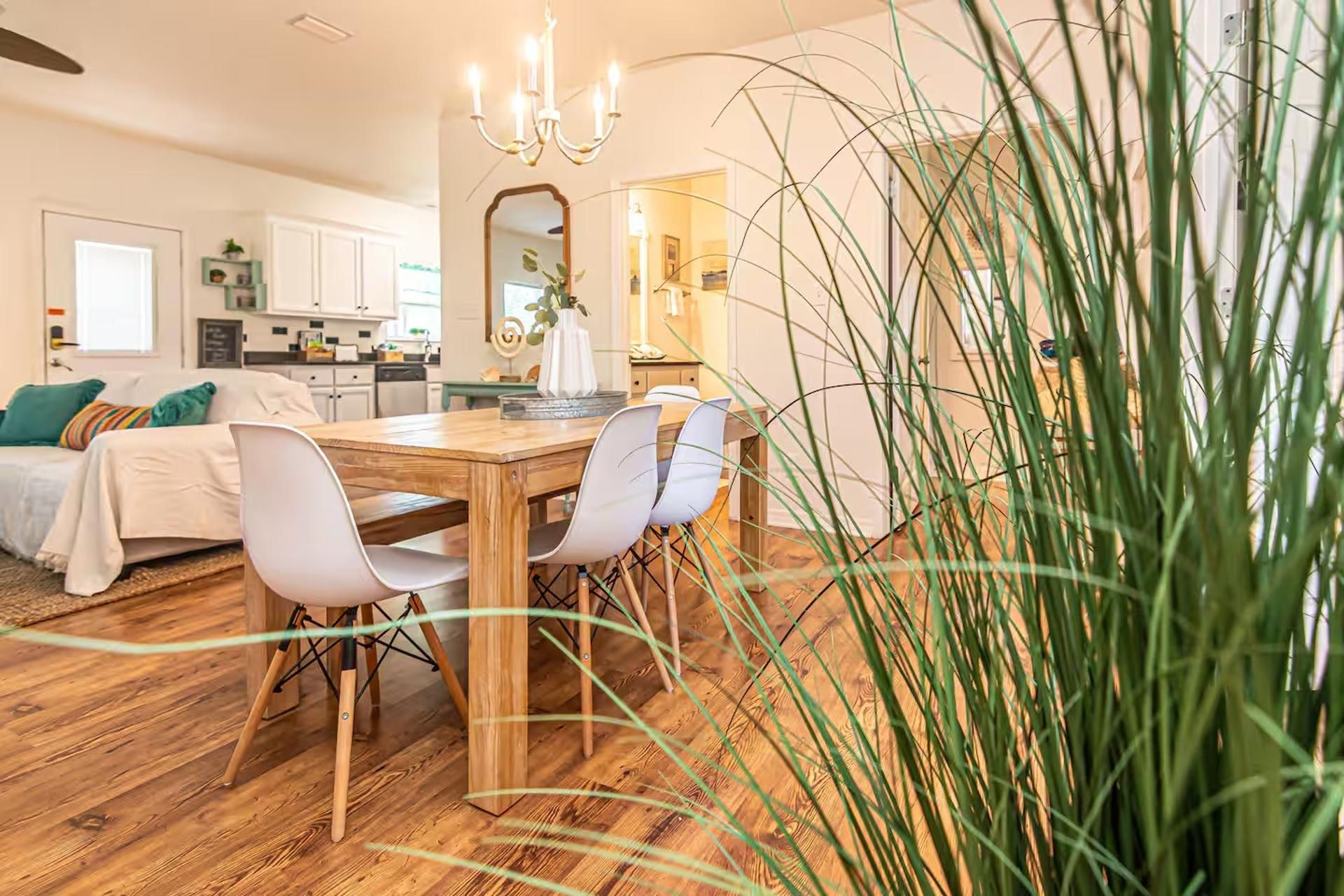 A dining area with a wooden table and chairs, a chandelier, and a large plant in the foreground.