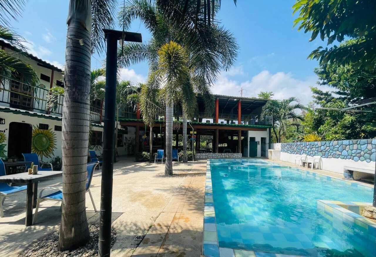 A swimming pool with lounge chairs, palm trees, and a building with a covered patio area.