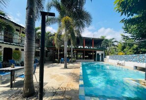 Una piscina con sillas de descanso, palmeras y un edificio con un patio techado.