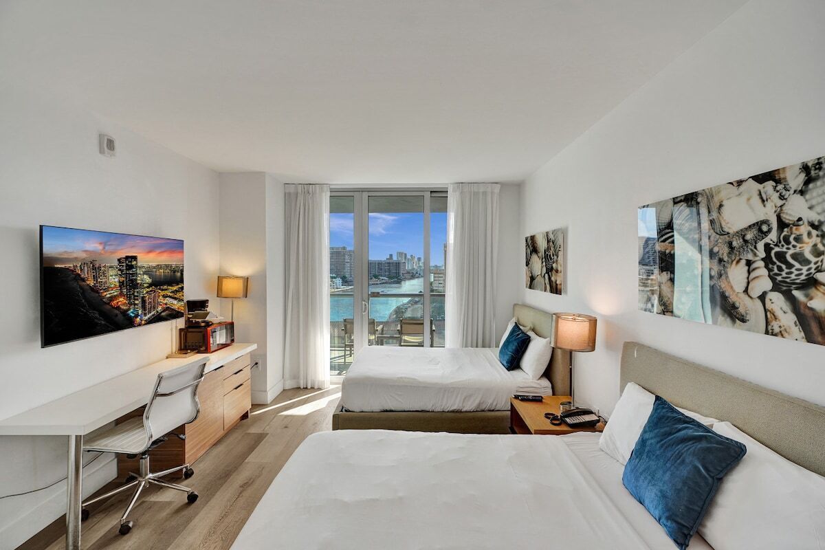 Ein Hotelzimmer mit zwei Betten, einem Schreibtisch und Blick auf Stadt und Wasser.