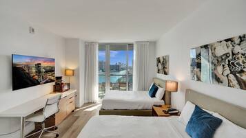 A hotel room with two beds, a desk, and a view of a cityscape and water.
