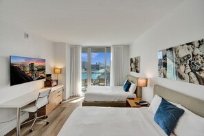 Ein Hotelzimmer mit zwei Betten, einem Schreibtisch und Blick auf Stadt und Wasser.
