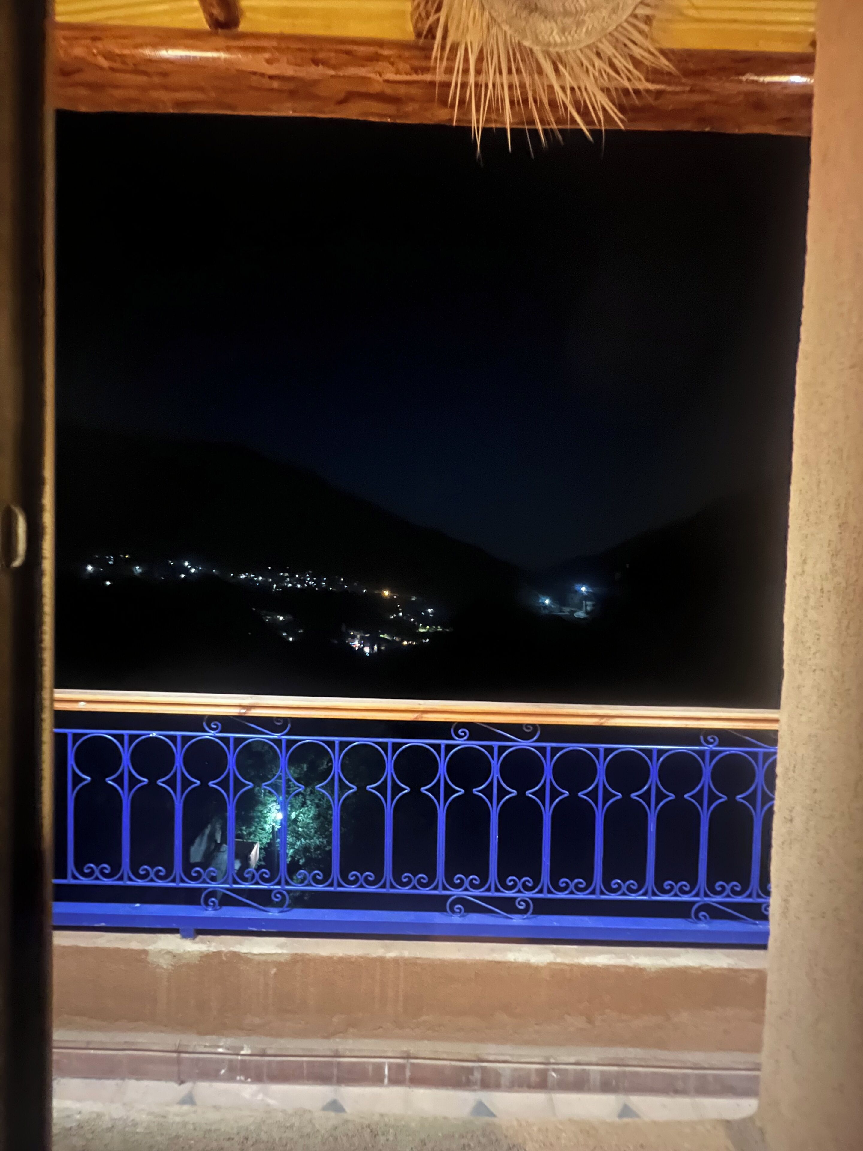 Vista nocturna desde un balcón con barandilla, con vistas a un paisaje urbano con luces y colinas.