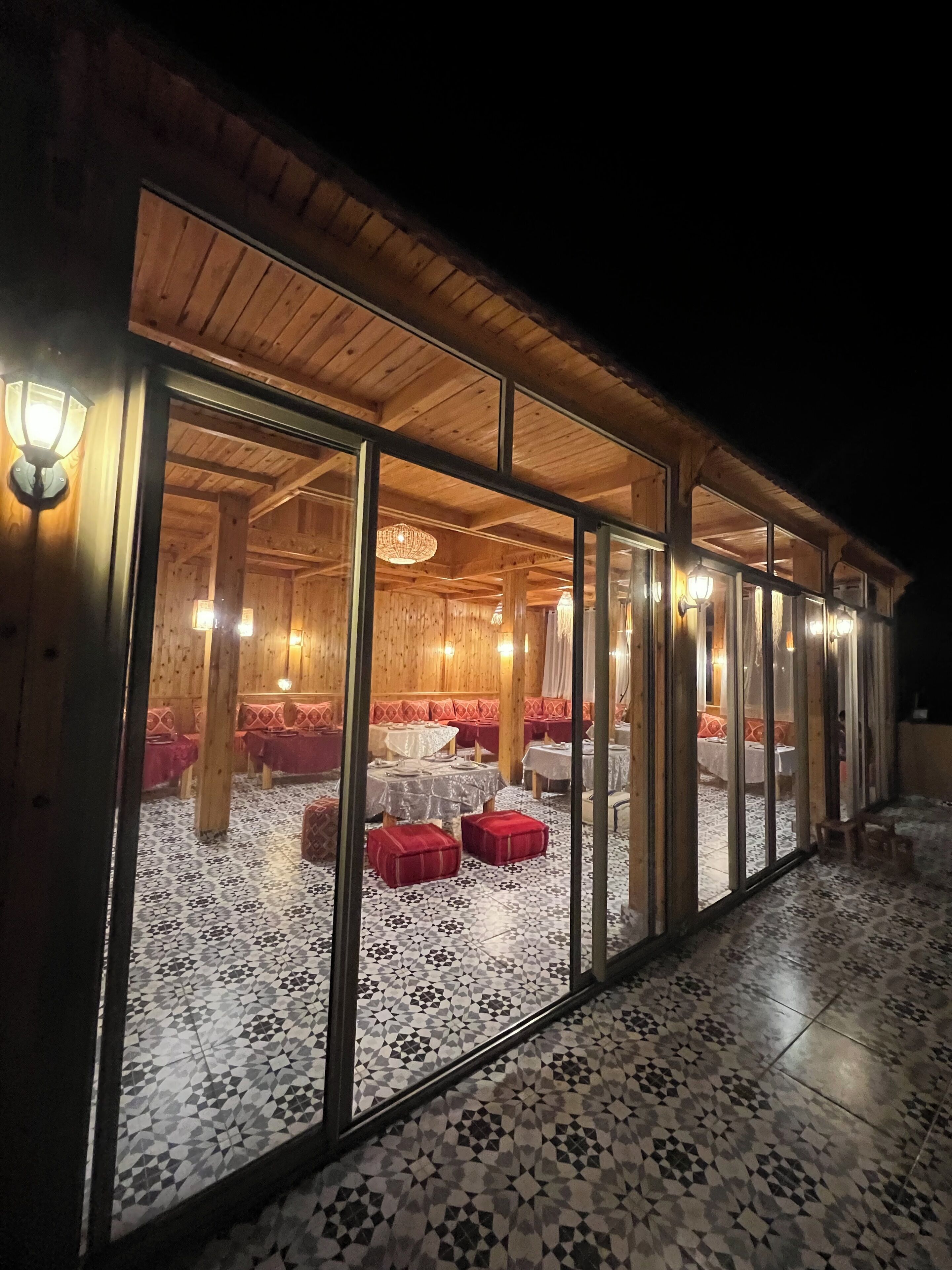 Un bâtiment en bois doté de grandes portes vitrées, d’un éclairage intérieur et d’un revêtement de sol à motifs.