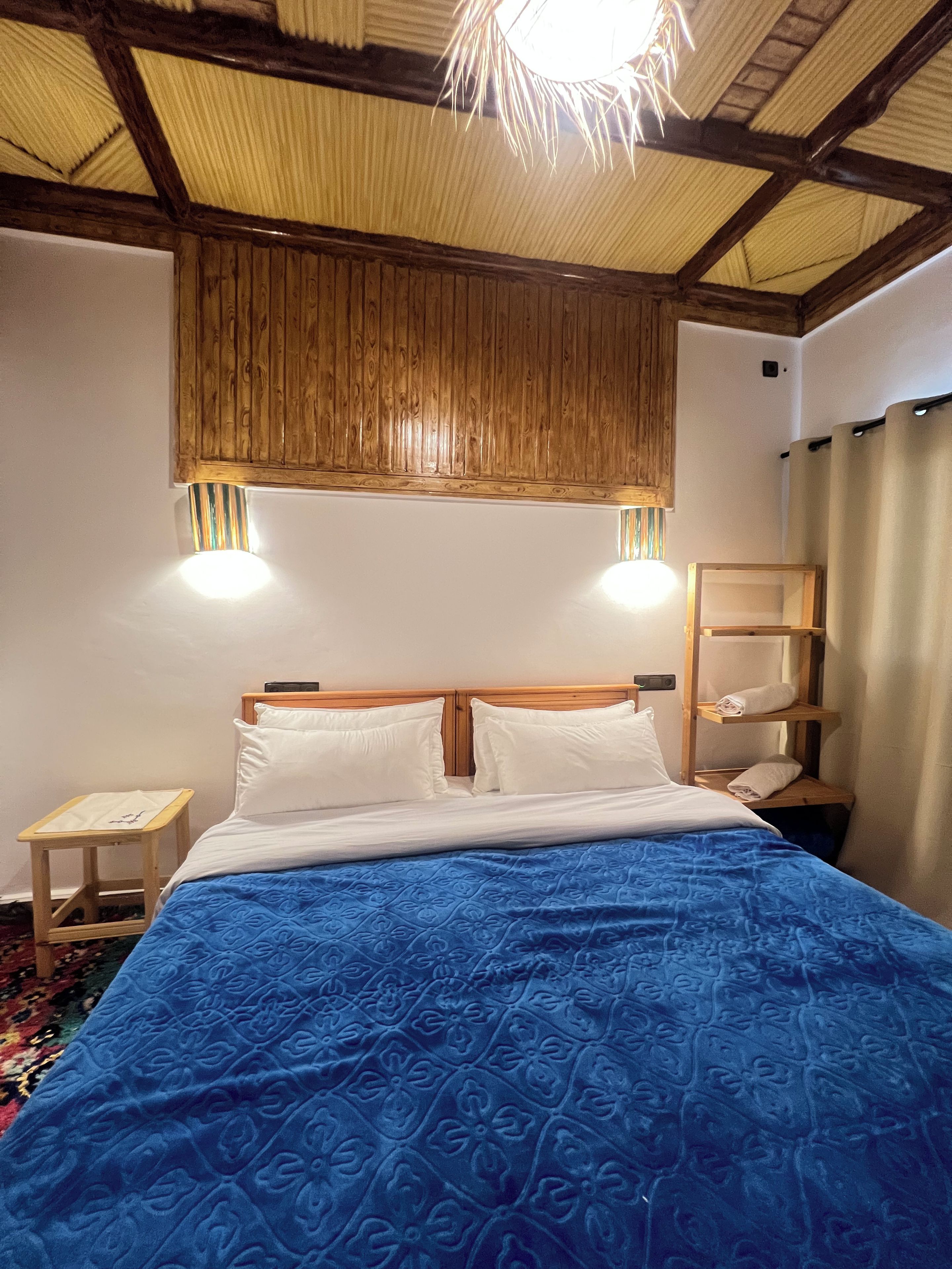 Une chambre à coucher avec une tête de lit en bois, une couvre-lit bleue à motifs, une table de chevet et un luminaire suspendu.