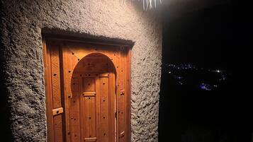 Une porte en bois surmontée d’une arche décorative, intégrée dans un mur de pierres à la texture particulière, et qui donne sur un escalier.