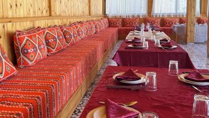 A long wooden bench with patterned cushions, a table set with plates, glasses, and cutlery, and a patterned floor.