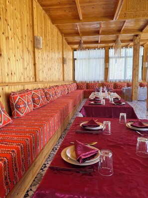 A long wooden bench with patterned cushions, a table set with plates, glasses, and cutlery, and a patterned floor.